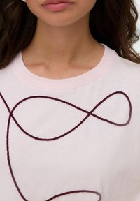 Světle růžové bavlněné tričko s tmavě burgundským smyčkovým designem. Krátké rukávy s žebrovaným kulatým výstřihem, hladká textura.