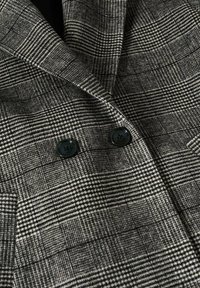 Tissu de manteau à carreaux gris et noir présentant un tissage texturé, avec deux boutons noirs à l'avant et un col au design net.