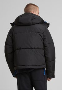 Černá péřová bunda s kapucí, horizontálním prošíváním a modrými šňůrkami. Materiál je lesklý s hladkým povrchem.