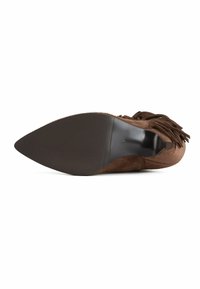 Zapato de ante marrón con punta afilada y tacón fino, con detalles de flecos y suela de goma texturizada. El interior es suave.