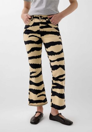 Beige flared jeans dengan garis-garis harimau hitam yang mencolok. Terbuat dari katun, dilengkapi dengan kantong depan dan hem yang dijahit dekoratif.