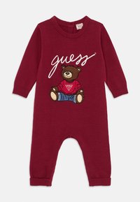 Combinaison en tricot bordeaux avec des manches longues, présentant un ours brodé portant une chemise rouge et un jean bleu, avec le mot "guess" en blanc.