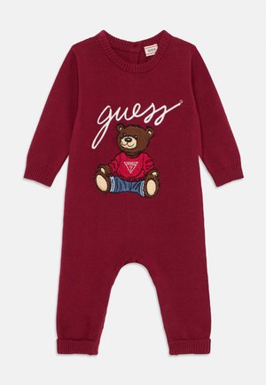 Burgunderfarget strikket heldress med lange ermer, prydet med en brodert bjørn iført rød skjorte og blå jeans, og ordet "guess" i hvitt.