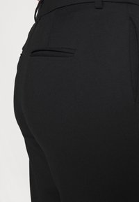 Svarta skräddarsydda byxor med en slät yta, smal passform och en diskret detalj på bakfickan. Midjan är fint avslutad.