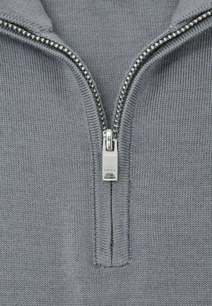 Close-up of silver zipper on grey knitted fabric, zipper pull engraved with "REISS" brand name.