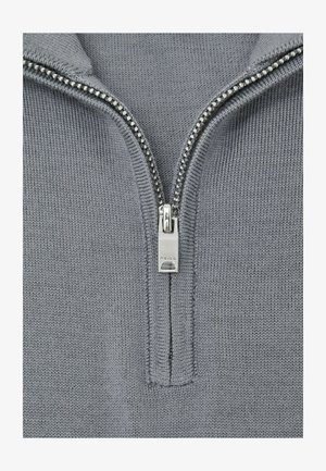 Nahaufnahme eines silbernen Reißverschlusses auf grauem Strickstoff, der Zipper-Schieber ist mit dem Markennamen "REISS" graviert.