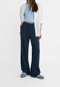Granatowe spodnie szerokie z elastycznym paskiem i sznurkiem. W połączeniu z jasnoniebieską dopasowaną bluzką i białą koszulą na guziki. Niebieskie sneakersy.