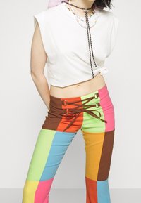 Haut court blanc avec un côté noué, associé à un pantalon patchwork multicolore comportant des sections vertes, orange, bleues et roses.