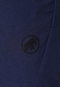 Donkerblauwe stof met een zwart wollen mammoetlogo binnen een cirkel, licht textuurrijk en aan de rechterkant gevouwen.