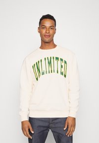 Cremefarbener Sweatshirt mit grünem "UNLIMITED"-Slogan. Verfügt über einen runden Halsausschnitt und gerippte Bündchen, besteht aus weichem, strukturiertem Material.