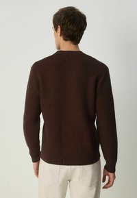 Burgundi värvi kootud sviiter, millel on tekstureeritud muster, ümar kaelus ja soonikkoes mansetid, kombineeritud heledate pükstega.