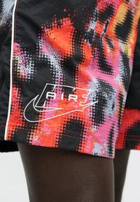 Μαύρο σορτς με πολύχρωμο, πουα μοτίβο σε πορτοκαλί, ροζ και γκρι. Περιλαμβάνει λευκό λογότυπο Nike και διακοσμητική ραφή.