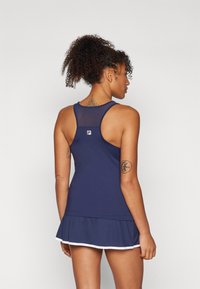 Marineblå tennisdress med en tettsittende tanktopp, mesh-bakside og plisserte skjørt. Har hvite detaljer langs kanten og et logo merke.