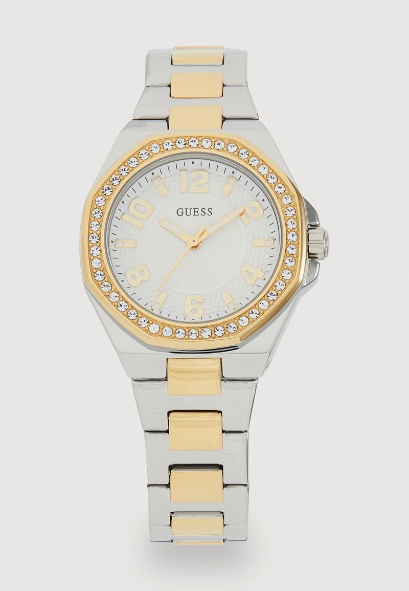 Rustfrit stål ur med ottekantet urskive, guldfarvede accenter og krystaludsmykninger. Hvid urskive med gyldne timemarkører og visere.