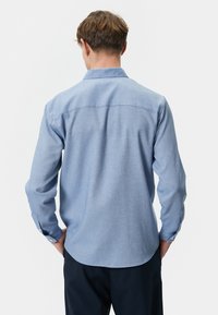 Lichtblauw, lange mouwen, overhemd met knoopsluiting, met een soepele textuur, knopen bij de manchetten en een afgeronde zoom. Design van de achternaad is minimaal.