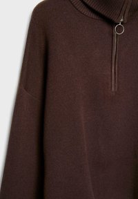 Brauner Pullover mit hohem Kragen und halblanger Reißverschlussöffnung, weichem Material und lockerer Passform. Besitzt einen dezenten gerippten Kragen und weite Ärmel.