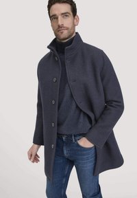 Marineblaue Wollmischung Jacke mit hohem Kragen, Knöpfen vorne und lässigem Schnitt. Getragen über einem passenden Rollkragenpullover, kombiniert mit blauen Jeans.