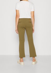 Pantalones de campana verde oliva con una textura suave, que presentan dos bolsillos traseros con sutiles acentos metálicos. Con una camiseta blanca.
