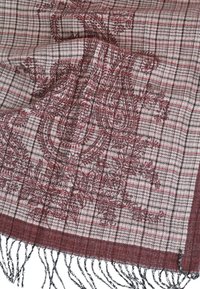 Sciarpa rossa e beige con motivo a scacchi, dettagli paisley, bordi sfrangiati e una consistenza morbida. Il materiale sembra essere tessuto.