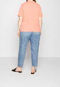 Korallfärgad t-shirt med kort ärm, avslappnad passform, tillsammans med ljusblå jeans. Svarta klackslip-ons med låg klack. Enkel design, utan mönster.