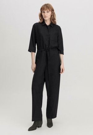 Zwarte jumpsuit met lange mouwen, knoopsluiting, een borstzak en een verstelbare trekkoord taille; ontwerp met wijde pijpen en een gladde textuur.