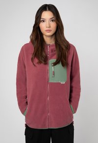 Bordeaux fleece hoodie met een groene borstzak; beschikt over een ritssluiting en een zachte textuur. Zoom en manchetten in contrasterend groen.