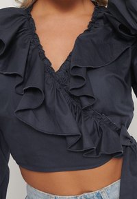 Top corto blu navy con dettagli arricciati lungo il collo e le maniche, con texture gathers e design a profondo scollo a V.