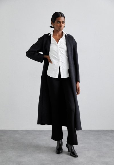 Long dark gray coat over a white shirt, paired with black pants and high-heeled black boots. Smooth fabrics and tailored fit.