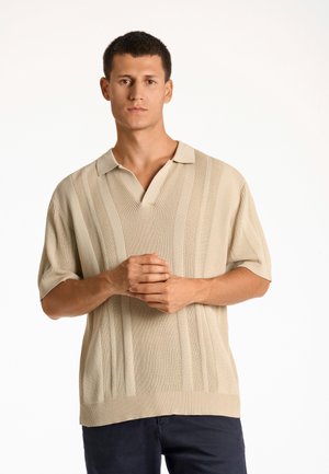 Beżowa koszulka polo z krótkim rękawem o prążkowanej teksturze i wzorze w pionowe paski, z dekoltem w serek i luźnym krojem.