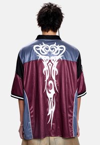 Chemise à manches courtes avec un schéma de couleurs bordeaux et gris, ornée d'un grand motif tribal blanc dans le dos et d'accents rayés.