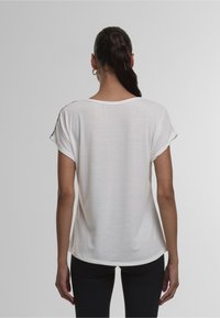 Camiseta blanca de manga corta con dobladillo redondeado, hecha de una tela ligera; presenta un diseño simple y un ajuste ligeramente relajado.