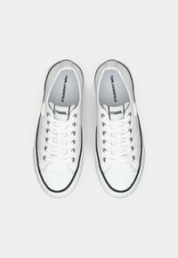 Λευκά πάνινα παπούτσια με μαύρες λεπτομέρειες και λαστιχένιες σόλες. Διαθέτουν στρογγυλή μύτη, δέσιμο με κορδόνια και λογότυπο στη γλώσσα και στην εσωτερική σόλα.