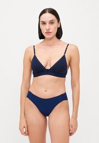 Bralette en coton bleu marine avec des bonnets triangulaires et des bretelles réglables, associé à un bas de bikini taille basse assorti, avec une texture lisse.