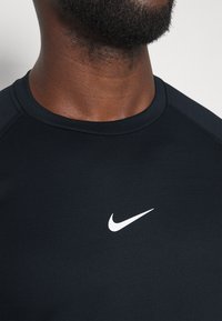 Detailní záběr na krk a horní část hrudi osoby, která má na sobě černé tričko Nike s bílým logem swoosh na hrudi.