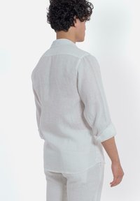 Witte linnen blouse met een ontspannen pasvorm, voorzien van een afgeronde zoom, opgeknoopte mouwen en een klassieke kraag, gezien vanuit de achterkant.