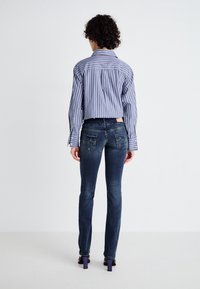 Chemise bleue et blanche à rayures, à manches larges, associée à un jean skinny bleu foncé avec poches arrière et coutures discrètes.