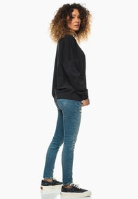 Svart oversized sweatshirt med ribbade cuffs, matchad med ljusblå skinny jeans och mönstrade svarta sneakers med vita sulor.