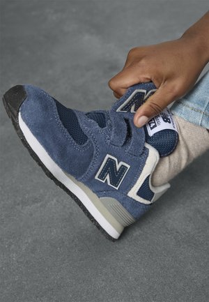 Marineblå semsket sneaker med mesh-paneler, har justerbar stropp, hvite og grå aksenter, samt en teksturert svart gummisåle.