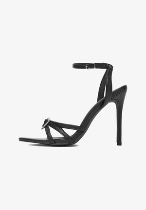 Juodos juostelės su aukštakulniu sandalais su plona kulkšnies dirželiu, smailu pirštu ir dekoratyviniu kalnų krištolo detalėmis priekyje. Lygios odos tekstūra.