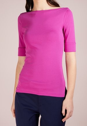 Přiléhavý krátký top v jasně růžové barvě s širokým výstřihem a hladkou texturou, doplněný tmavě modrými kalhotami.