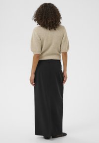 Pull en tricot beige avec des manches bouffantes associé à une longue jupe noire. La jupe présente une texture lisse et une coupe sur mesure.