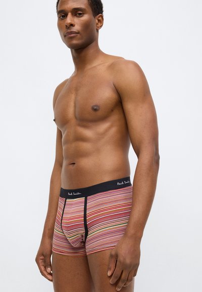 Ριγέ μποξέρ σε κόκκινο, κίτρινο και πράσινο με μαύρη ελαστική μέση που φέρει το όνομα της μάρκας. Βαμβακερό ύφασμα, εφαρμοστή σχεδίαση.