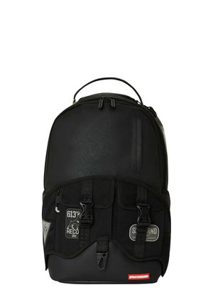 Mochila negra con tela texturizada, correas ajustables, dos hebillas en la parte frontal y parches con logotipo. Compartimento principal con cremallera y bolsillo lateral.