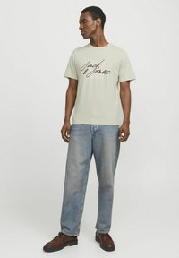 Lichtgroene t-shirt met korte mouwen met het "Jack & Jones" logo in donkerbruin. Gecombineerd met losse blauwe jeans en bruine schoenen.