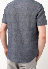 Chemise bleue à manches courtes en tissu texturé, avec un ourlet arrondi et des coutures renforcées au niveau du col et des coutures d'épaule.