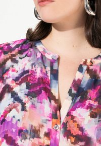 Blusa colorata con un motivo astratto vivace in tonalità di rosa, viola e blu. Dispone di una chiusura con bottoni e una trama di tessuto morbido.