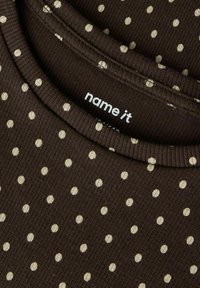 Brun bomullsskjorte med ribbet tekstur, med kremfargede polkadotter og rund halslinning. Merkeetikett synlig inne i kragen.