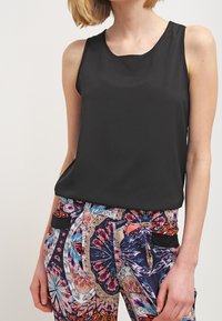 Top negro sin mangas hecho de una tela suave, con un escote redondo. Combinado con unos pantalones vibrantes con estampados que muestran diseños florales y colores.