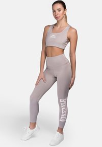 Top corto atlético gris claro y leggings de cintura alta, con un logo blanco en la pierna, hechos de un material liso y elástico.