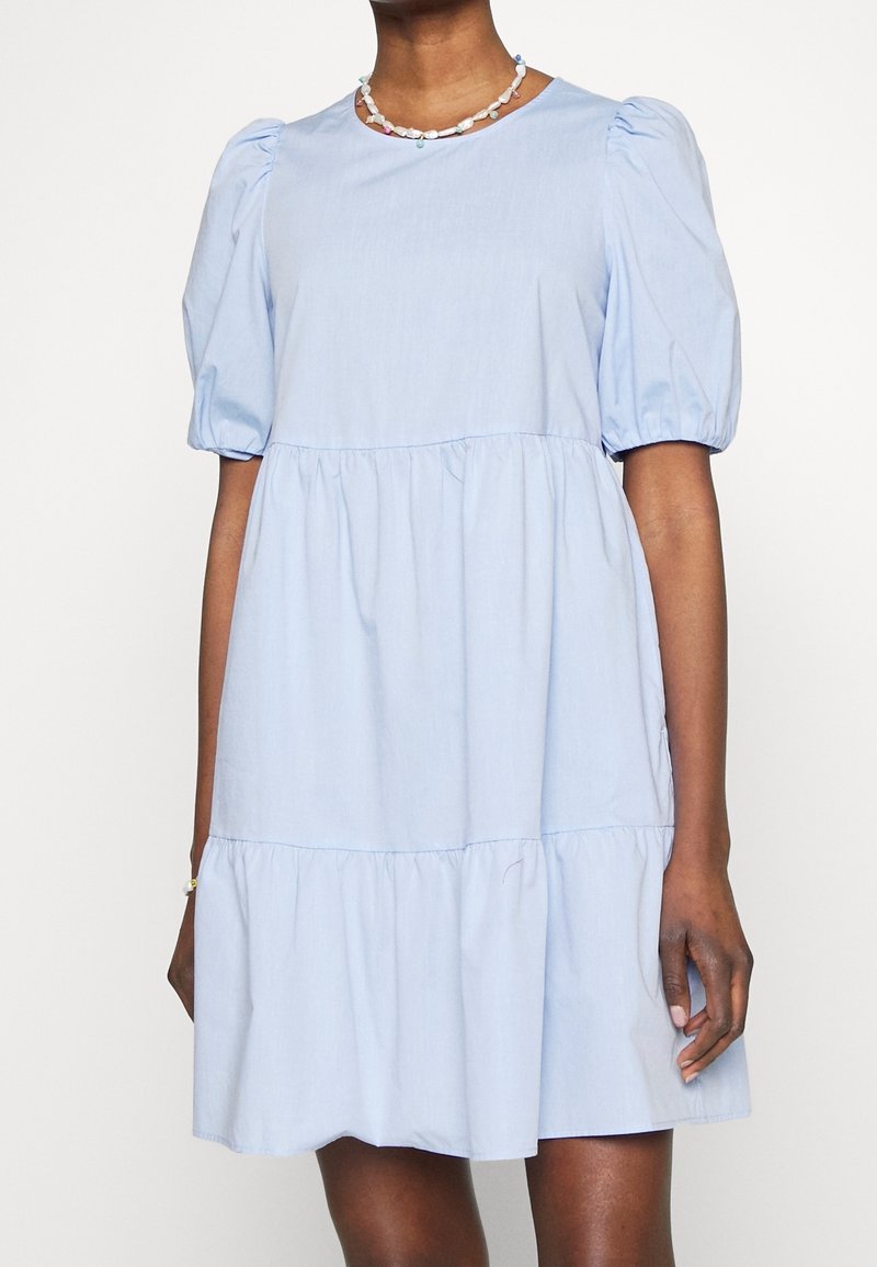Světlé modré šaty s krátkým rukávem, nabíranými rukávy, nabíranými volány na lemu a kulatým výstřihem vyrobené z měkké, strukturované tkaniny.